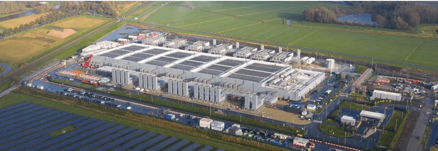 Vista aérea de campus de data center con paneles solares adyacentes; toma vertical tipo dron.