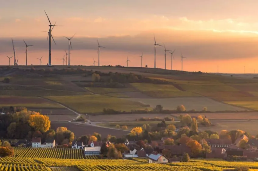 Se muestra un paisaje rural enfocado en la producción de energía renovable y agricultura con múltiples aerogeneradores en la parte superior de las colinas.
