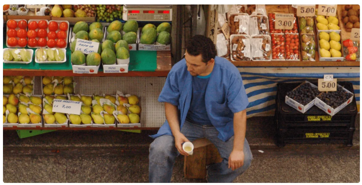 Se muestra un puesto de frutas en un mercado al aire libre o de abastos con un vendedor descansando.