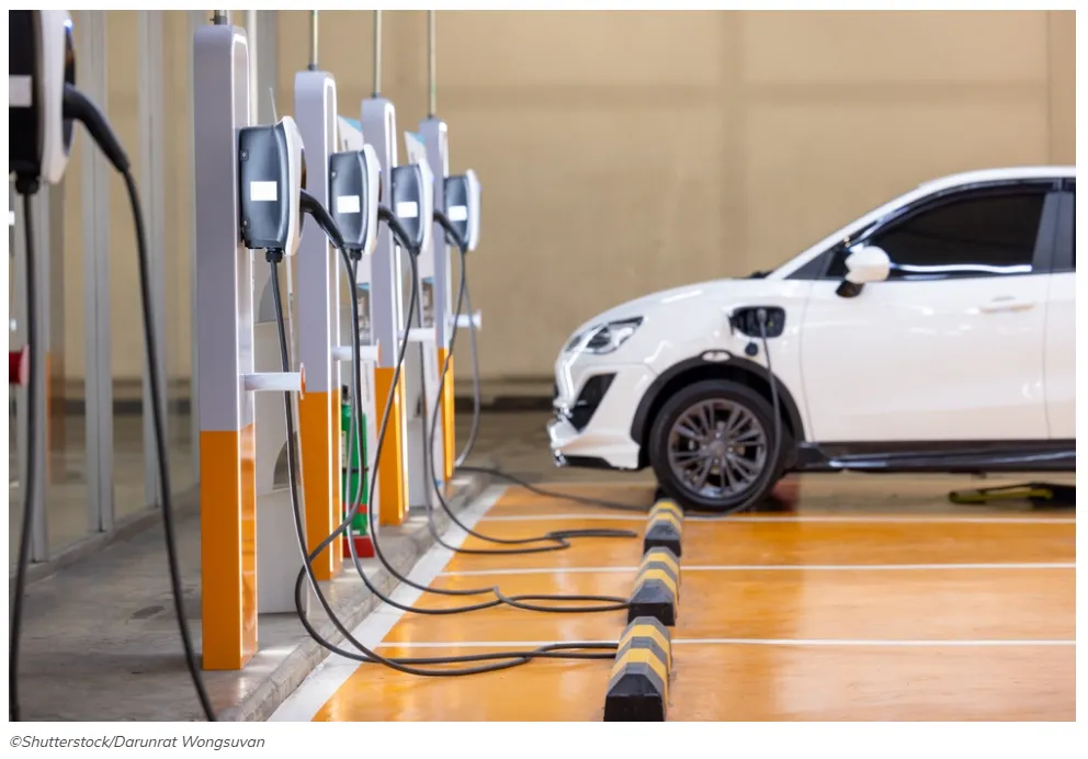 Esta imagen muestra un vehículo eléctrico blanco enchufado a una estación de carga de pared.