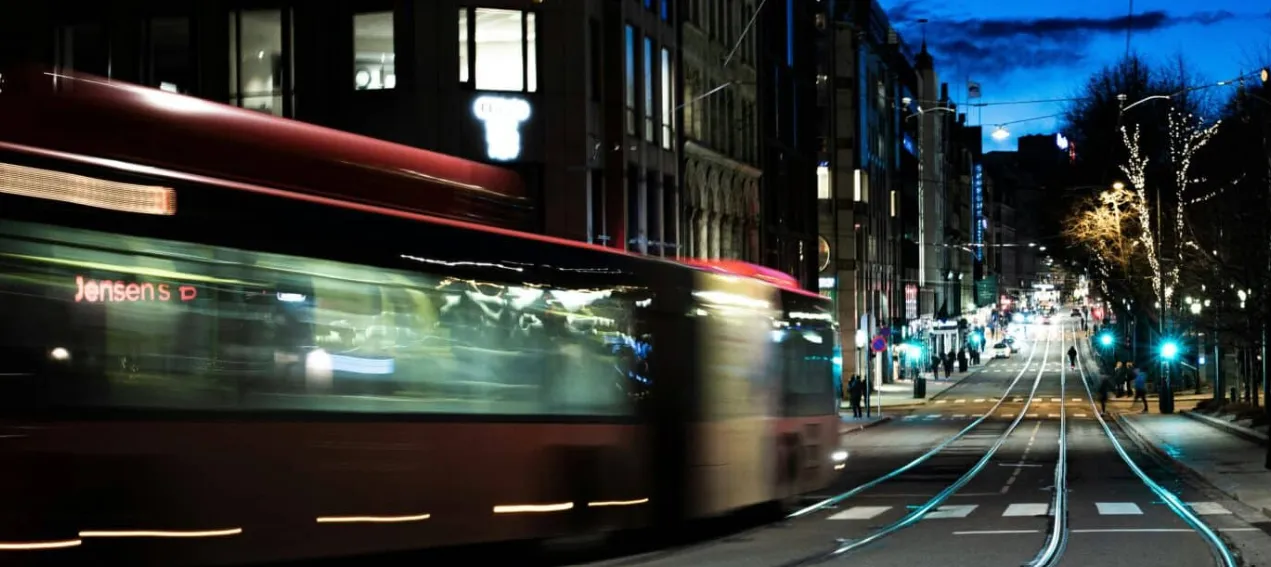 Esta imagen muestra un tranvía rojo pasando rápidamente por una calle en Oslo durante la noche.