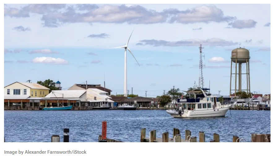 Esta imagen muestra el puerto de Crisfield, Maryland, conocido como la "Capital mundial del cangrejo". El paisaje incluye un aerogenerador prominente y una torre de agua elevada cerca de la línea costera.